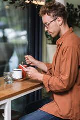 blurred young man in glasses holding spoon and texting on smartphone in cafe