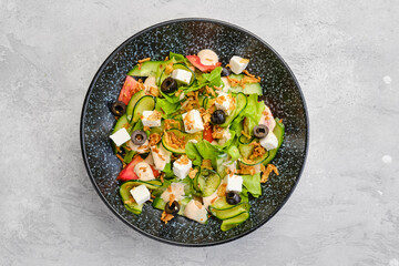 Top view of salad with lettuce, cucumber, olives, tomato, feta and bacon chips