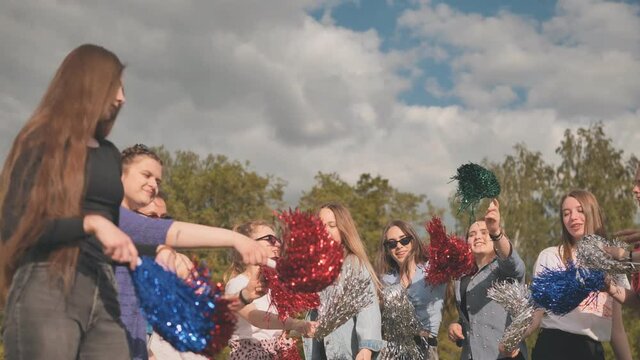 Cheerful girls in the meadow waving multi-colored pompoms.