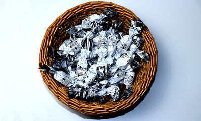 White and silver packaged Christmas chocolate candies in a brown wicker basket on a white background
