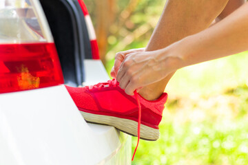 Women's hands in the forest near the car against the background of green trees on a bright summer sunny day tie the laces of sneakers. Selective focus