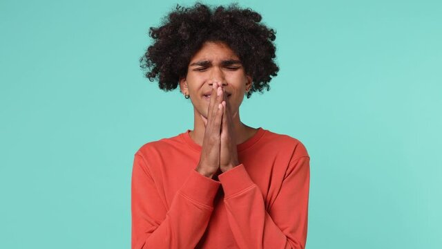 Tired exhausted sad young curly african american man 20s wears azure t-shirt look camera covering hiding face with hands looking up above isolated on plain pastel light blue background studio portrait