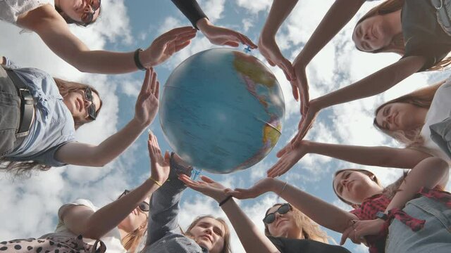 Earth conservation concept. 11 girls surround the rotating earth globe with their palms.