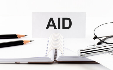 AID on paper card,pen, pencils, glasses,financial documentation on table - business concept