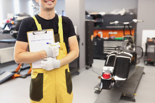 Auto mechanic in workshop holds clipboard for taking orders closeup