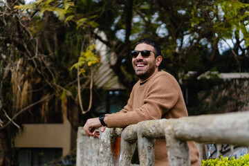 young latin hispanic man smiling leaning on a railing in autumn