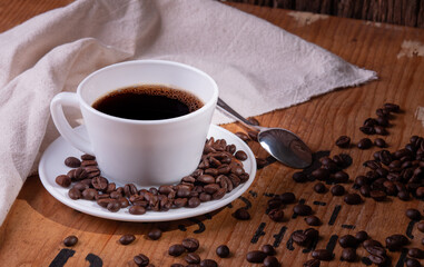 side view of white coffee cup and organic coffee beans on vintage pine wood table top with side light shining on area. cafe concept on photography image.