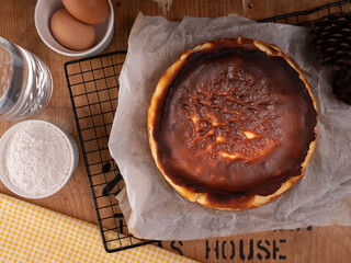 Basque burnt cheesecake placed on a black pastry rack with some ingredient, flour and eggs on vintage wood table. food concept on photography image.