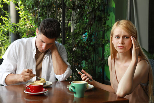 Young woman with smartphone ignoring her boyfriend in outdoor cafe. Boring date
