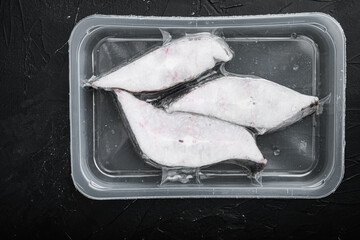 Raw fillets frozen halibut airtight vacuum pack, on black dark stone table background, top view...