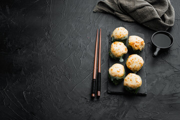 Baked sushi maki rolls with salmon, crab, cucumber, avocado, flying fish roe and spicy sauce, on black stone background , with copyspace  and space for text