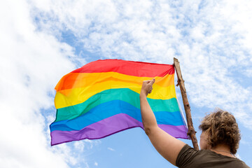 Unrecognizable sideways woman, waving a rainbow flag. Raising a clenched fist