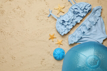Light blue beach ball, toy, starfishes and swimsuit on sand, flat lay. Space for text