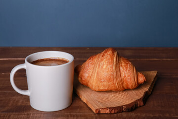 Fresh baked croissant, craft wooden chopping board, mug of black coffee on rustic brown table. Cup of hot drink, bakery food. Breakfast, morning menu, cafe concept. Side view
