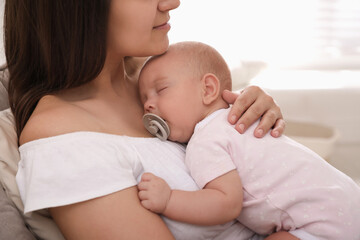 Happy young mother with her sleeping baby on chair  at home, closeup