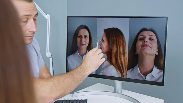 Plastic surgeon consulting woman about facial lift surgery, while pointing at computer screen and showing types of facelift and nose correcting procedures