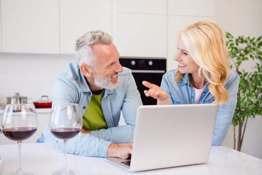 Photo of two smiling cheerful people married couple talking have conversation browsing laptop surfing online drink wine