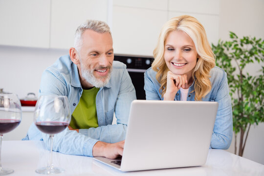 Photo of charming sweet mature lovers dressed jeans shirt drinking wine watching modern gadget smiling indoors room home