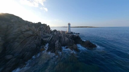 FPV video, view from above, stunning aerial view from an FPV drone flying at high speed over a rocky coastline with a lighthouse illuminated during a dramatic sunset. Faro di Capo Ferro, Sardinia. - Powered by Adobe