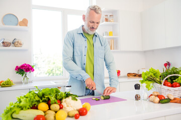 Photo of handsome charming mature man dressed jeans shirt cutting vegetables smiling indoors room home