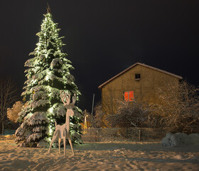 Snow covered outdoor Christmas tree with green lights and white artificially created reindeer at...