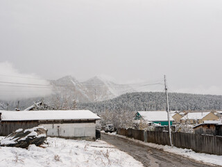 Chemal, Altai Republic, Russia - 15 October 2020: Russian rural village Chemal in the snow. Village street. Altai mountains are covered with snow and clouds.