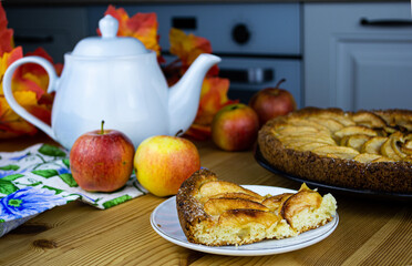 Homemade apple pie on curd dough. In the foreground is a piece of pie, apples, a teapot and an...