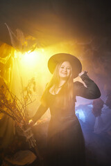 Young woman looking like witch having fun on Halloween in a dark room with yellow light and smoke. Carnival concept and Halloween party