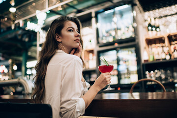 Contemplative female diva thoughtful looking away and thinking during cocktail time in local bar restaurant, Caucasian customer with alcohol beverage feeling pondering during weekend leisure in cafe