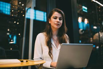 Portrait of skilled woman with modern laptop looking at camera while working remotely in cafe, Caucasian hipster girl with digital netbook posing spending day for doing distance job indoors