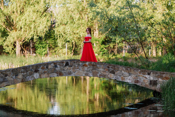 Redhead woman in red dress walking on stone bridge