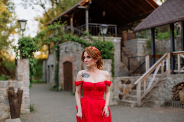 Portrait of attractive redhead tattooed woman in red dress and diadema on blurred medieval castle background