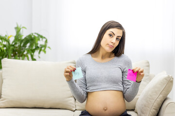 Photo of pregnant woman holding pink and blue papers which mean gender of future baby.