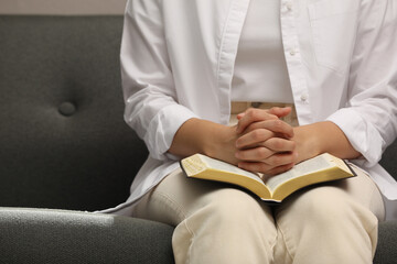 Religious woman praying over Bible indoors, closeup