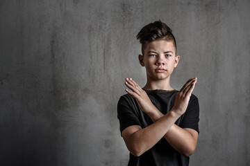 Sad boy teenager standing on a dark background crossed his arms on his chest with a stop sign. Problems of suppression of emotional detachment and isolation of adolescent children. Difficulties growin