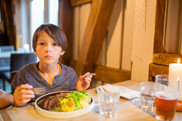 Preschool child, cute boy, eating lamb meat in a restaurant, cozy atmosphere, local small restaurant in Tromso