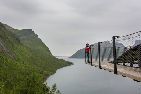 Child, standing on the edge of a 44 meter long viewing platform, overlooking the water of Bergsfjord, enjoying view on Senja island, Norway.