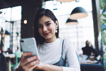 Cheerful woman browsing smartphone in cafe