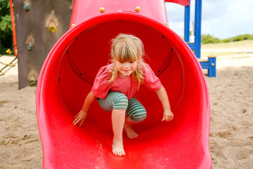 Little preschool girl playing on outdoor playground. Happy toddler child climbing and having fun...