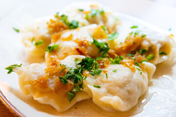 Delicious homemade polish dumplings stuffed with meats and caramelized onions on top served in white plate.
