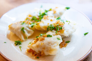 Delicious homemade polish dumplings stuffed with meats and caramelized onions on top served in white plate.