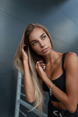 Fototapeta premium Beauty portrait of fashion sexual caucasian woman model with pretty face in black tank top with silver bracelet near a black metal building in the city