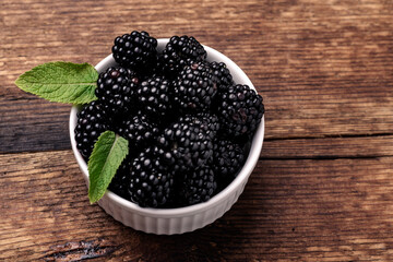 Blackberries in a white bowl with mint leaves on a wooden background close-up.
