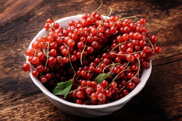 Red currants in a deep plate on a wooden background.
