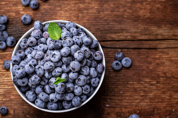 Fresh blueberries in a bowl on a brown wooden background.