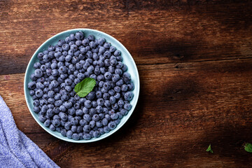 Fresh blueberries berries in a plate on a dark wooden background.