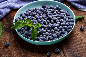 Fresh blueberries berries in a plate on a dark wooden background.