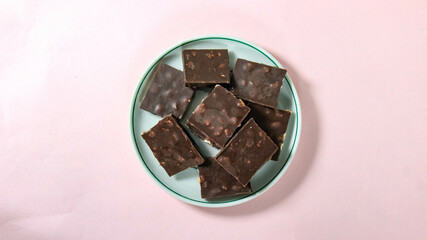 A chocolate bar with nuts broken into pieces lies on a saucer.