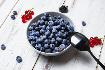 Fresh blueberries in a plate with a spoon on a white wooden background. Fruit, berry background, proper healthy nutrition, vegetarianism.