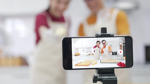 4K Asian couple bakery shop owner using smartphone with internet vlogging sweet dessert baking on social media together in the kitchen. Small business entrepreneur and online cooking class concept